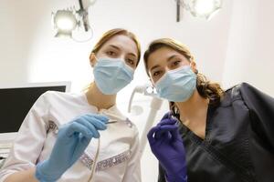 From below female dentists with mirror and device bending over patient during appointment in dental clinic. photo