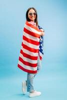 Young smiling happy woman wears casual clothes holding american flag and looking to the camera isolated on blue background photo