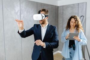 Man client wearing VR glasses imagining future interior standing with designer at the construction site. photo