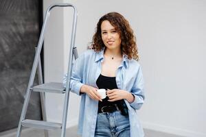 Cute girl designer takes a break from work and drinks coffee while standing in the room photo