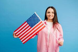 Young smiling happy woman wears casual clothes holding american flag and looking to the camera isolated on blue color background. photo