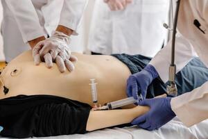 Doctors practicing cardiopulmonary resuscitation and intravenous injection on medical manikin photo