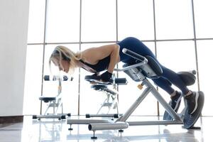 Woman performing back extension exercise using hyperextension bench in gym. photo