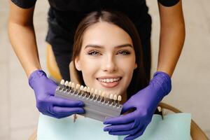 Dentist choosing teeth enamel shade color for young smiling female patient before whitening procedure. photo