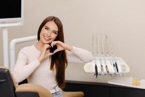 Patient is smiling, gesturing hands heart in dentist office. photo