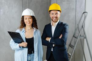 Attractive young contractor and customer standing in room in helmet and looking at camera. photo