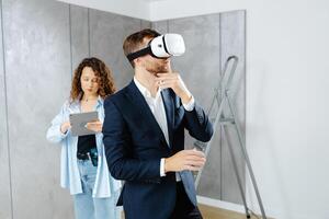 Man client wearing VR glasses imagining future interior standing with designer at the construction site photo