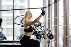 Athletic woman resting on bench after exercising with dumbbells in gym photo