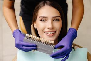 Dentist choosing teeth enamel shade color for young smiling female patient before whitening procedure photo