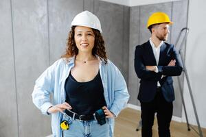 Attractive young contractor and customer standing in room in helmet and looking at camera photo