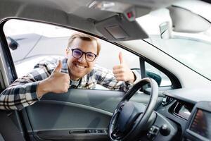 Man looking through window inside new car, checking it before purchase at modern dealership store. Cheerful guy buying or renting automobile at showroom photo