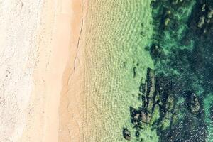 drone shot of sandy beach merging with rocky ocean floor. Aerial drone top down view. Background beach concept texture photo