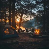 A tent and campfire are set up near a lake at sunset photo
