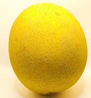 A whole ripe melon with a textured yellow rind, displaying an intricate webbed pattern. Its vibrant color and firm exterior indicate freshness, making it a delicious and nutritious tropical fruit. photo