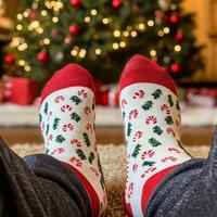 A person wearing christmas socks on the floor near a christmas tree photo