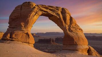 A natural rock arch framed by a colorful sunset in a desert landscape. photo