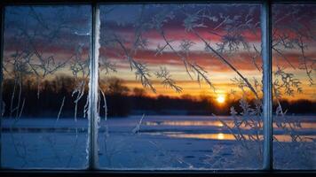 A frosty window frames a vibrant winter sunset over a snowy landscape. photo