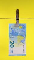 Twenty Euro Banknote Hanging on a Clothesline with Clothespin, 20 euro bill clipped with wooden peg on string against yellow background, concept of money laundering, Vertical footage video