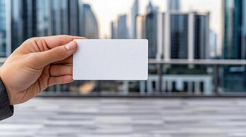 A person holding a blank business card in front of a cityscape photo