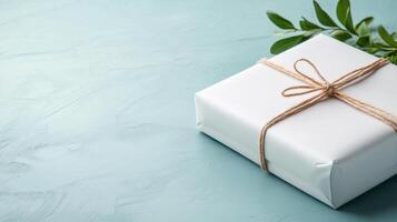Gift box with twine and green leaves on blue background photo