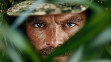 A man in camouflage is peeking out from behind some leaves photo