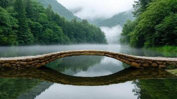 serene stone bridge arches over misty lake surrounded by lush greenery photo