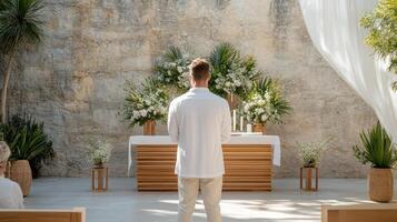 man white outfit stands front of beautifully arranged altar, surrounded by flowers and greenery photo
