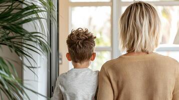 mother and child standing together, looking out window, feeling safe photo