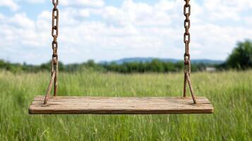 rustic wooden swing sways gently in grassy field under blue sky photo