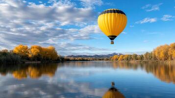 A yellow hot air balloon is flying over a lake photo
