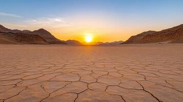The sun sets over a desert landscape with cracked ground photo