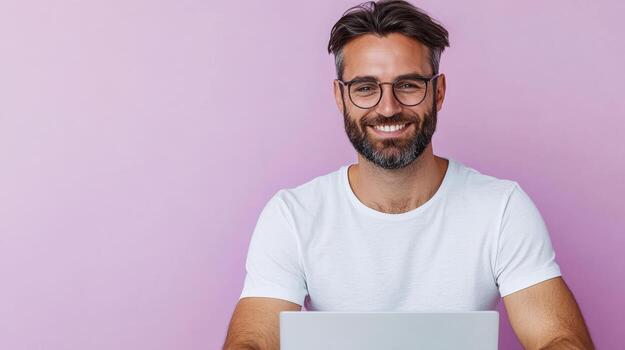A man with glasses and a beard is smiling while using a laptop photo