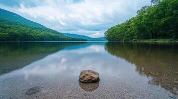 serene lakeside view with rock in foreground, surrounded by lush greenery and mountains photo