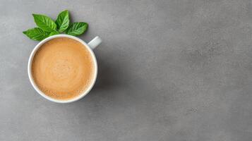 Aromatic coffee in white cup with fresh green leaves on gray stone surface photo