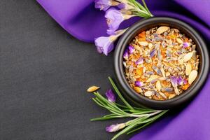Golden spice blend in a stone bowl surrounded by dried herbs and petals, elegantly displayed on dark grey linen with a rich texture photo