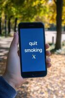 Hand holding smartphone displaying quit smoking message on screen in a park photo