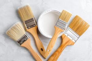 Paint brushes and open can of white paint lying on gray concrete background photo