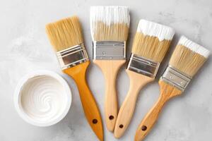 Paint brushes and open can with white paint lying on gray surface photo