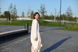 A woman with sunglasses smiles while standing against a modern building, creating a sense of urban sophistication. photo