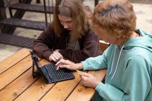 A happy mature grandmother with a granddaughter using a credit card is shopping online on a laptop. photo