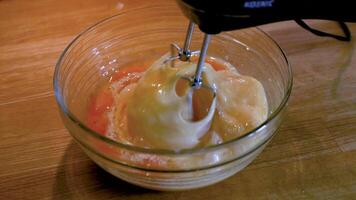Electric mixer whipping eggs into airy foam in glass bowl for dessert, cake batter or cream preparation. Closeup of frothy egg mixture swirls stirred rapidly under mixer beaters. Kitchen scene 01 video