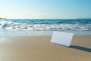 A blank card rests on sandy beach shore with ocean waves in the background. photo