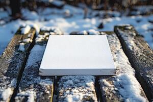 A blank canvas resting on a snow-covered wooden table in a winter landscape. photo