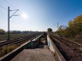 A pair of railway tracks extending into the distance under a bright blue sky, surrounded by autumn foliage and open fields, evoking a sense of travel and adventure. photo