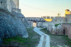 A historic fortress pathway lined with stone walls under warm evening sunlight. photo