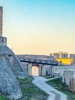 A stone fortress with historic walls and a scenic walkway under a golden sunset sky. photo
