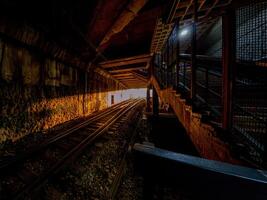 A dark underground railway tunnel illuminated by golden light at the exit, creating a striking contrast between shadow and brightness, evoking mystery and anticipation. photo