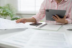 Digital Organization and Workflow. A woman engages with documents and a tablet in her home office, emphasizing modern financial management. photo