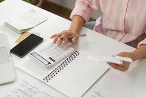 Finance and Calculation. A woman using a calculator and reviewing expenses in her home office. photo