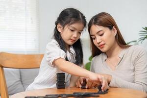 Connection and Playtime. A mother supporting her daughter as they play with dominoes together at the table. photo